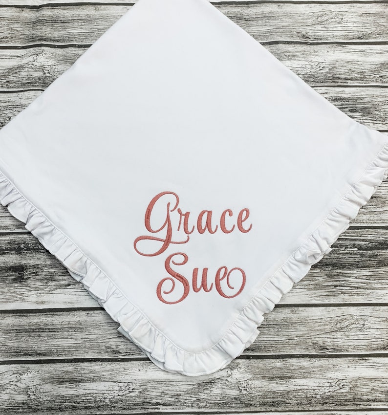 May include: White baby blanket with a ruffled edge and the name "Grace Sue" embroidered in pink.