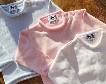 Puede incluir: Tres suéteres de punto en colores pastel, azul claro, rosa y blanco. Cada suéter tiene cuello redondo con tres botones en el hombro y una pequeña etiqueta. Los suéteres están hechos de tejido de punto texturizado.