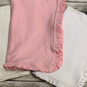 May include: Two baby blankets, one pink and one white, with ruffled edges. The pink blanket is folded on top of the white blanket.