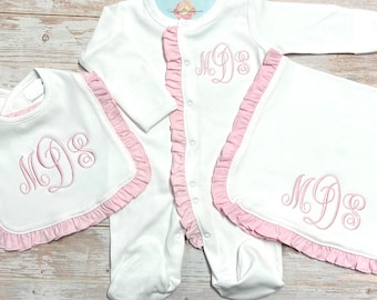 May include: A white baby onesie, bib, and blanket with pink ruffled trim. All three items are embroidered with the monogram "MDS" in pink thread.