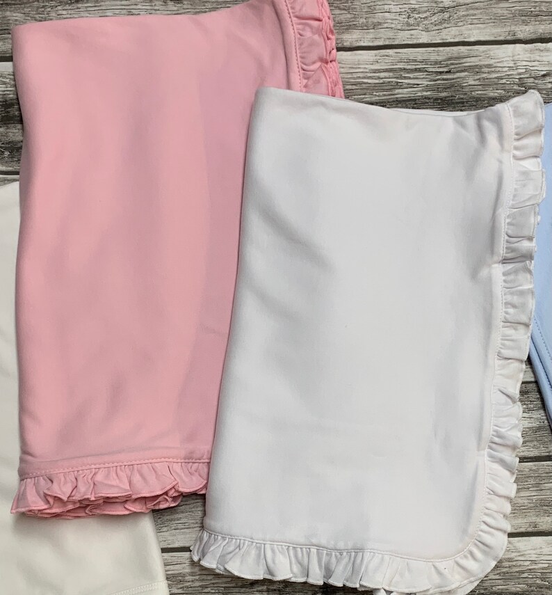 May include: Two baby blankets with ruffled edges. One is pink and the other is white.