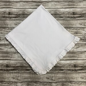 May include: A white baby blanket with a ruffled edge.
