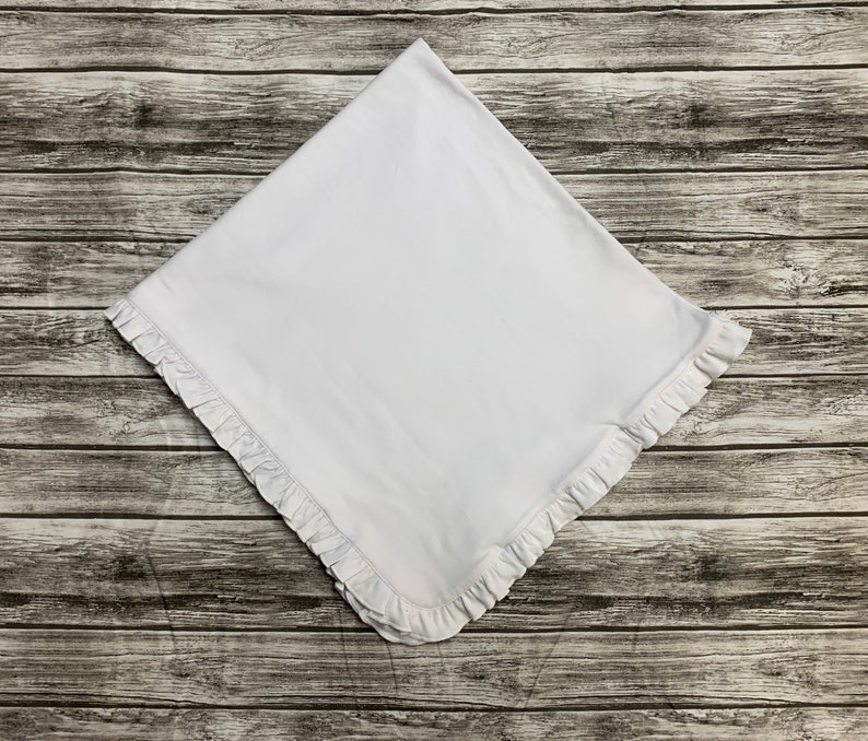 May include: A white baby blanket with a ruffled edge.