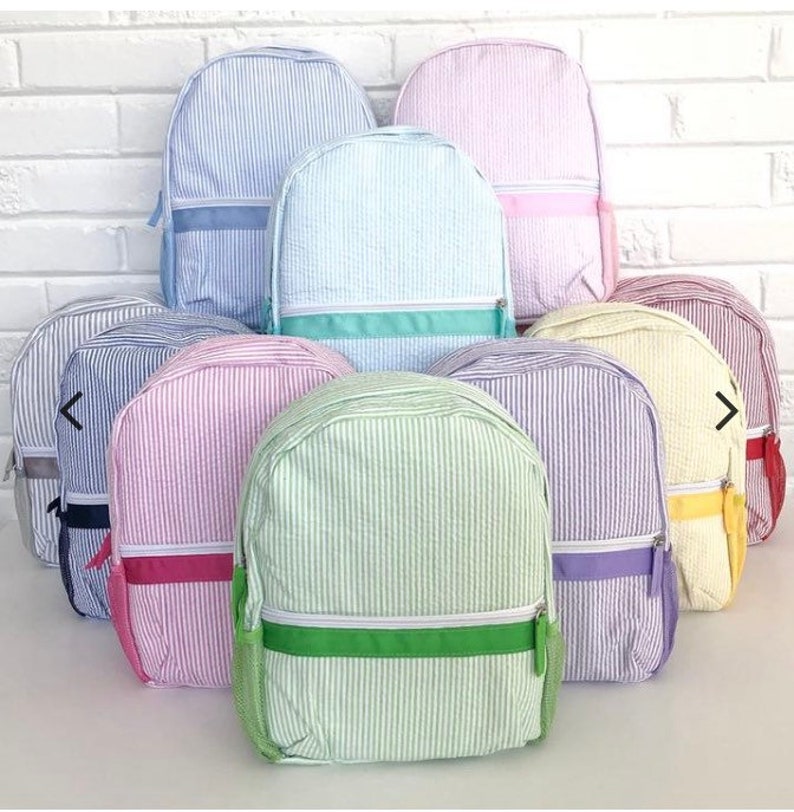 May include: A collection of seersucker backpacks in various pastel colors, including blue, pink, green, and yellow. Each backpack features a vertical striped pattern, a front zippered pocket, and a matching colored trim.