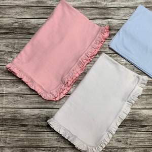 May include: Three baby blankets with ruffled edges. One is pink, one is white, and one is light blue.