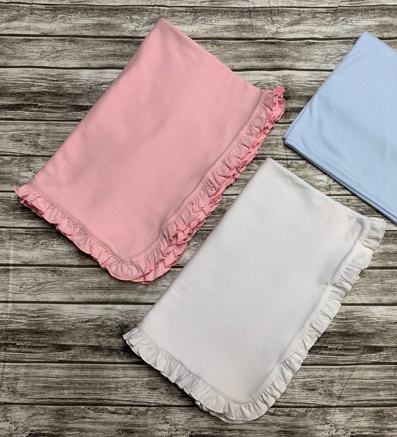 May include: Three baby blankets with ruffled edges. One is pink, one is white, and one is light blue.
