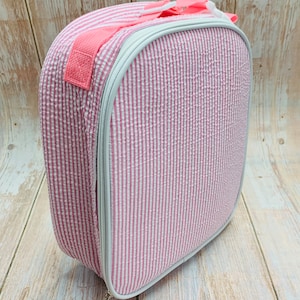 Op de afbeelding: Roze en wit gestreepte lunchtas met een ritssluiting en een roze handvat.