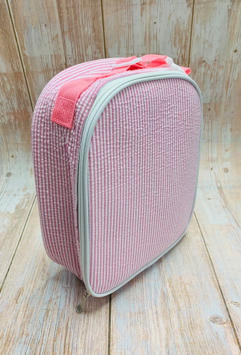 Op de afbeelding: Roze en wit gestreepte lunchtas met een ritssluiting en een roze handvat.