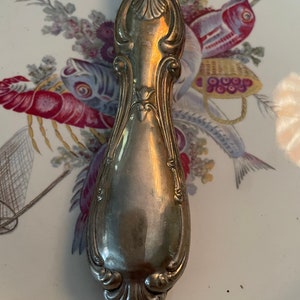 May include: A silver, ornate, decorative handle for a serving utensil. The handle is highly detailed with a floral design.