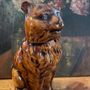 Peut inclure: Figurine en céramique marron représentant un ours assis, avec une finition brillante. L'ours a une texture de fourrure détaillée et regarde sur le côté. La figurine est probablement vintage et ajoute une touche de charme rustique à tout décor.