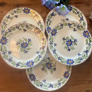 May include: Set of four white ceramic plates with a blue and green floral design. The plates have a gold rim and are perfect for a formal dinner setting.