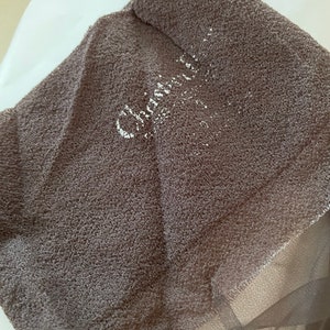 May include: A brown sheer fabric with a textured surface. The fabric has the word "Chloé" printed on it in white.
