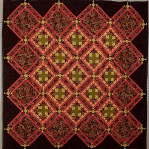 Może przedstawiać: Kołdra z geometrycznym wzorem kwadratów i rombów. Kołdra jest wykonana z tkaniny w odcieniach brązu, różu i żółci.