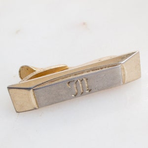 Może przedstawiać: Złoty i srebrny klips do krawata z wygrawerowanymi inicjałami "J.I.".