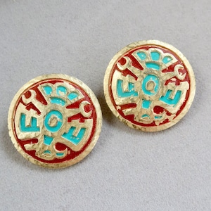 May include: A pair of gold-tone earrings with a red and turquoise design. The earrings are round and feature a stylised geometric pattern.