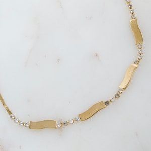May include: A gold chain necklace with small clear rhinestones and four wavy gold bars.