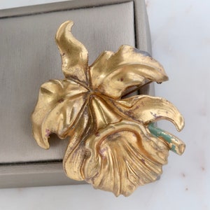 May include: A gold-toned metal flower brooch with a green stem. The flower has a detailed design with multiple petals.
