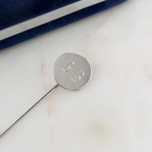 Op de afbeelding: Een zilveren stickpin met een ronde, zilveren bovenkant. De bovenkant is gegraveerd met de initialen "BB".