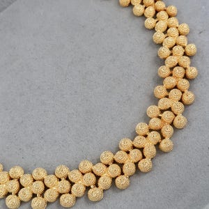 Peut inclure: Un collier doré avec une chaîne composée de petites perles rondes texturées.