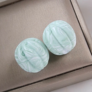 May include: A pair of green and white swirl patterned round earrings. The earrings are in a jewelry box.
