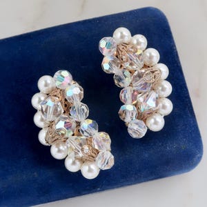 May include: A pair of iridescent crystal and pearl earrings. The earrings are shaped like a crescent moon and are made with small, faceted crystals and large, white pearls.