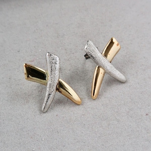 以下が含まれることがあります： X字型のシルバーとゴールドのイヤリングのペア。イヤリングはテクスチャ加工が施され、モダンなデザインです。