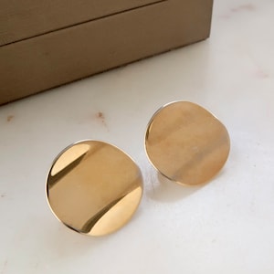May include: A pair of gold-toned, round, disc-shaped earrings.