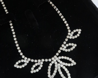May include: A silver necklace with a delicate design of leaves made of clear rhinestones. The necklace is displayed on a black velvet background.