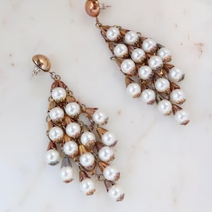 May include: A pair of vintage chandelier earrings. Each earring features a cascade of white faux pearls suspended from a copper-toned metal frame. The earrings have a post-back closure and a detailed design.