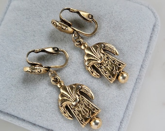 May include: A pair of gold tone clip-on earrings with ornate, detailed,  rectangular pendants. The pendants have a scalloped top and a textured design.