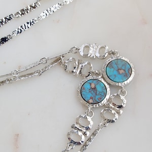 May include: A silver chain necklace with two turquoise blue round stones. The chain is made of small, textured links.