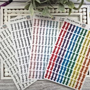 May include: A collection of sticker sheets with the days of the week printed in various colors. The stickers are arranged on a white tray with a wooden background. The text "Days of the Week-19" is visible on some sheets.