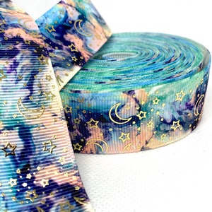 May include: A roll of blue, green and pink ribbon with a white background and gold foil stars and crescent moons.