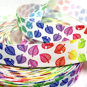 May include: Rainbow coloured ribbon with a white background and a repeating pattern of green leaves. The ribbon is rolled up and stacked on top of itself.