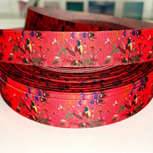 May include: Red ribbon with a floral and bird print. The ribbon is rolled up and the print is visible on the top and bottom of the roll.