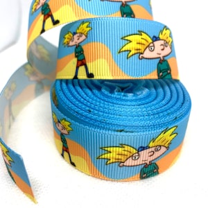 May include: Blue and yellow ribbon with a cartoon character of a boy with spiky blond hair. The character is wearing a green shirt and red shorts.