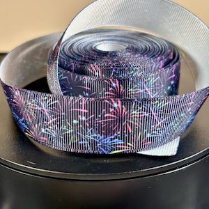 May include: A roll of black and white ribbon with a colorful firework pattern. The ribbon is on a black surface.