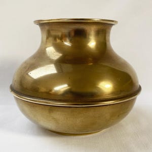 Op de afbeelding: Een vintage messing vaas met een afgeronde body en een uitlopende rand. De vaas heeft een warme, gouden tint en een glad, reflecterend oppervlak. Het ontwerp bevat een duidelijke band in het midden. Dit decoratieve stuk is geschikt voor woondecoratie.