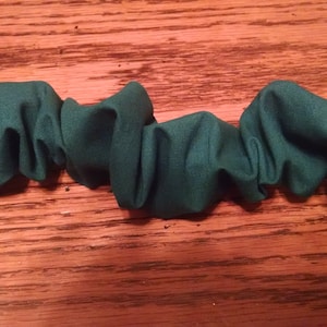 May include: A long strip of teal fabric is gathered and bunched up, creating a wavy, undulating pattern. The fabric is soft and appears to be made of a lightweight material.