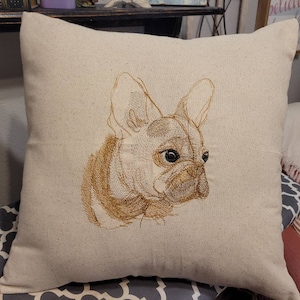 May include: A beige pillow with an embroidered image of a French Bulldog. The dog is facing the right side of the pillow and has brown fur.