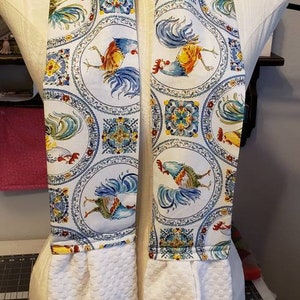 May include: Two white kitchen towels with a blue and white rooster pattern. The towels are attached to a white fabric loop.