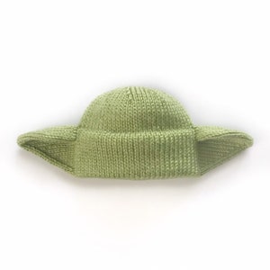 May include: A green knitted hat with large, pointed ears. The hat is made of a soft, textured yarn and has a simple, classic design.
