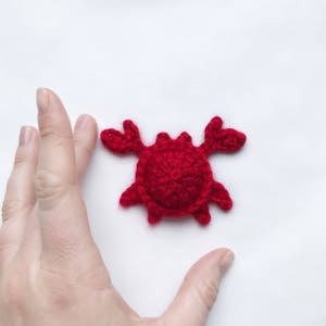 May include: A small red crocheted crab with a detailed shell and claws.