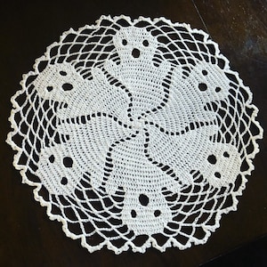 May include: White crocheted doily with a circular design featuring five ghost shapes.