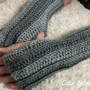 May include: A pair of gray fingerless gloves made with a textured crochet stitch. The gloves are shown on a white fuzzy surface. The text "Color: Bistro" is visible in the lower right corner of the image.