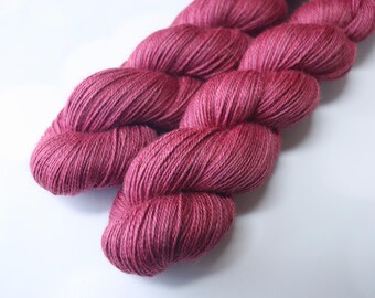 May include: A skein of vibrant, deep rose-colored yarn. The yarn is tightly spun, with visible individual strands, and is arranged in a twisted, compact bundle. The color is consistent throughout, suggesting a high-quality dye. Ideal for knitting or crochet projects.