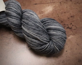 May include: A skein of gray yarn with varying shades of gray and white. The yarn is tightly wound and appears soft. The yarn is likely used for knitting or crocheting projects.