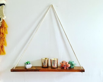 May include: A wooden shelf hangs from the ceiling with white ropes. The shelf is decorated with two gold candle holders, a small potted succulent, and two small animal figurines.