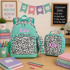 May include: A mint green and white dalmatian print backpack, lunch bag, and pencil case set. Each item features the name Kaia in pink lettering. The backpack has a front pocket, the lunch bag has a top handle, and the pencil case is cylindrical.