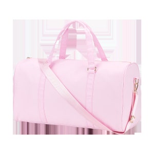 May include: A light pink canvas duffel bag with a long adjustable shoulder strap and gold hardware.